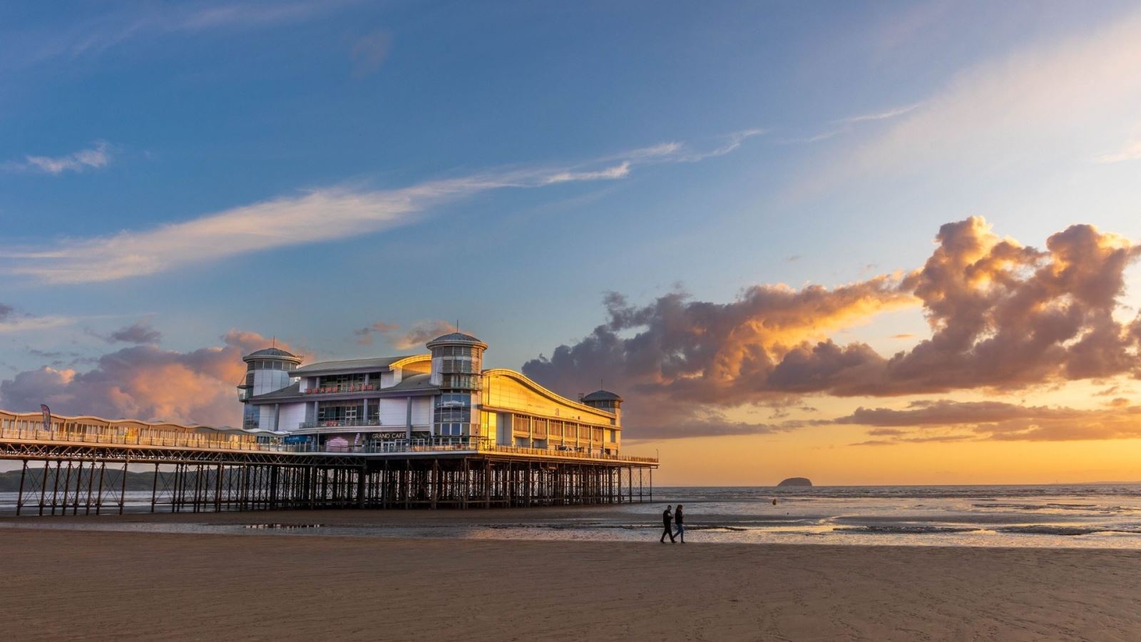 Two people walking on the shoreline past the Grand Pier in Weston-super-Mare at sunset